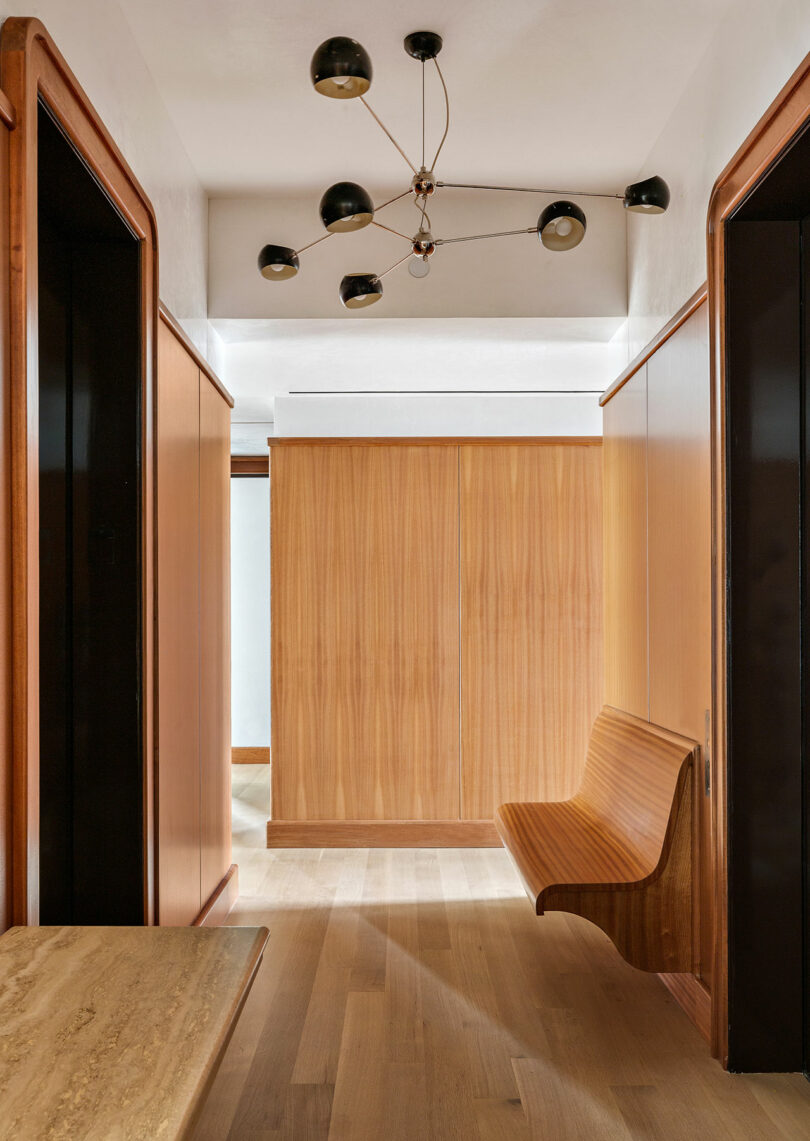 Modern hallway featuring light wood panels, a unique wooden bench, and a stylish black ceiling light fixture.