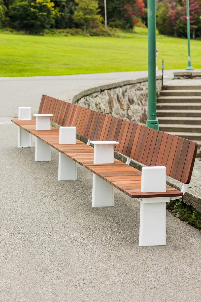 A wooden bench with white metal supports in a park with green grass and a path.