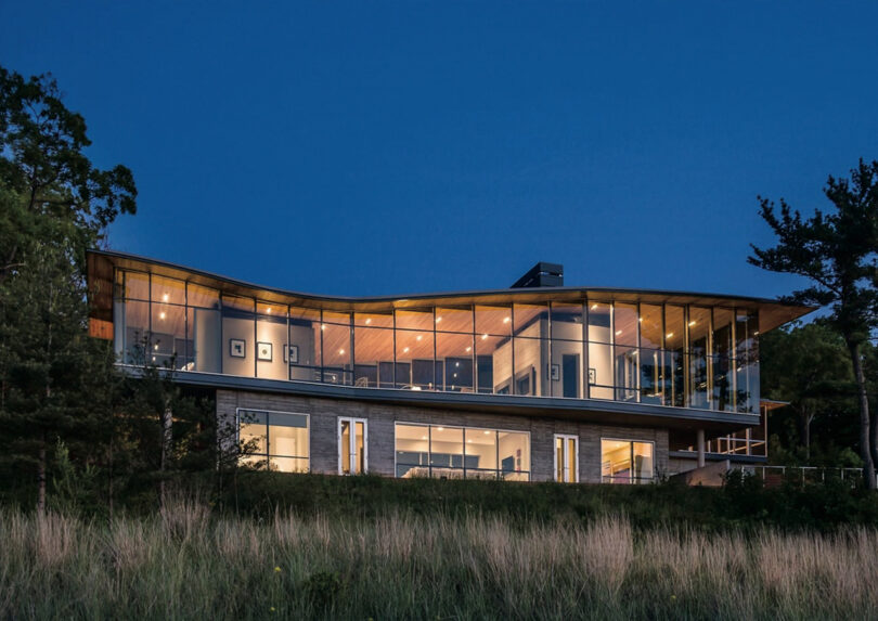 Modern glass-walled house illuminated at dusk.