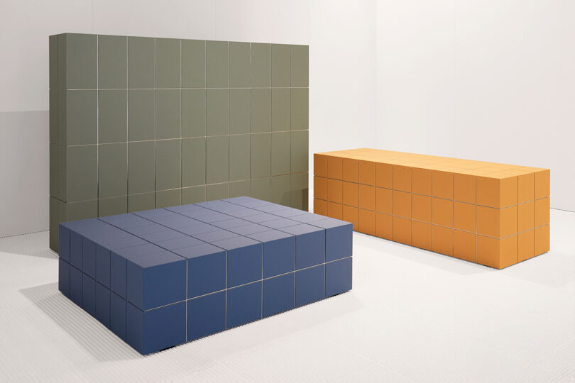 Three rectangular modular benches in green, blue, and orange, in a white room.