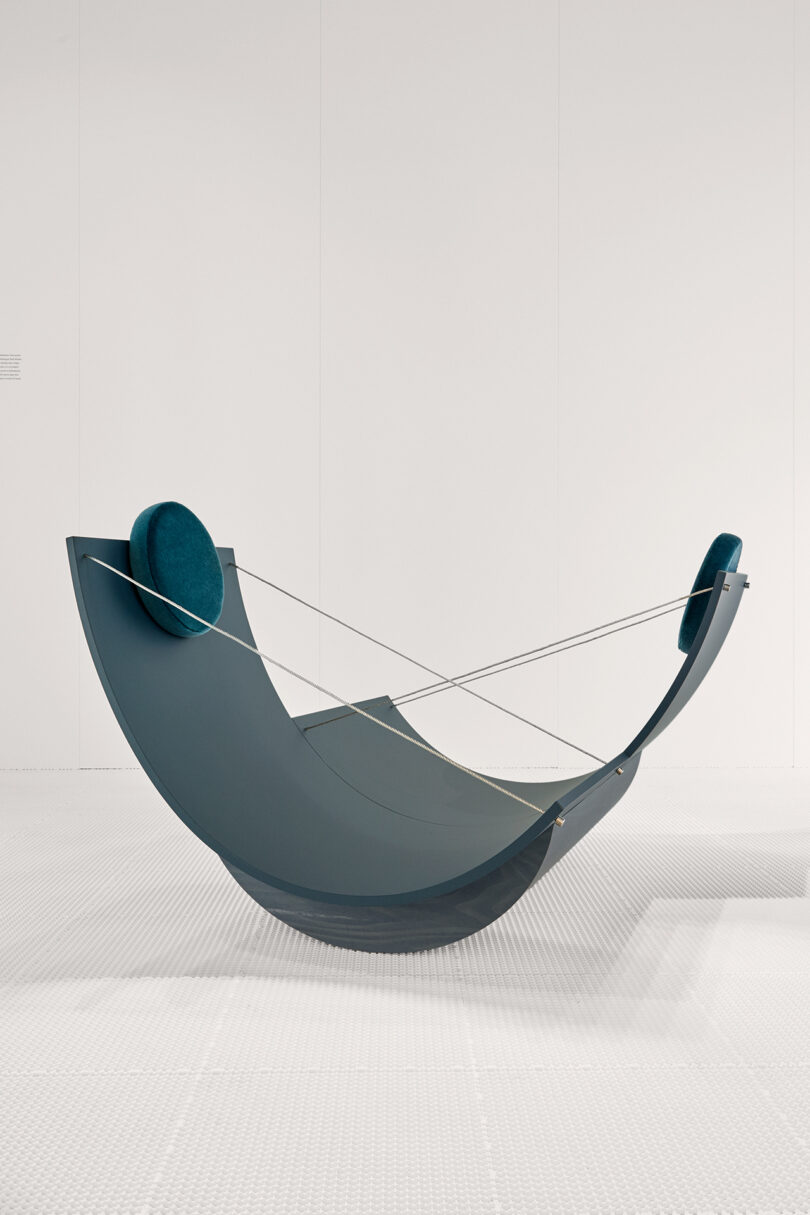 Hammock made of dark blue and silver materials, displayed in a white gallery space.