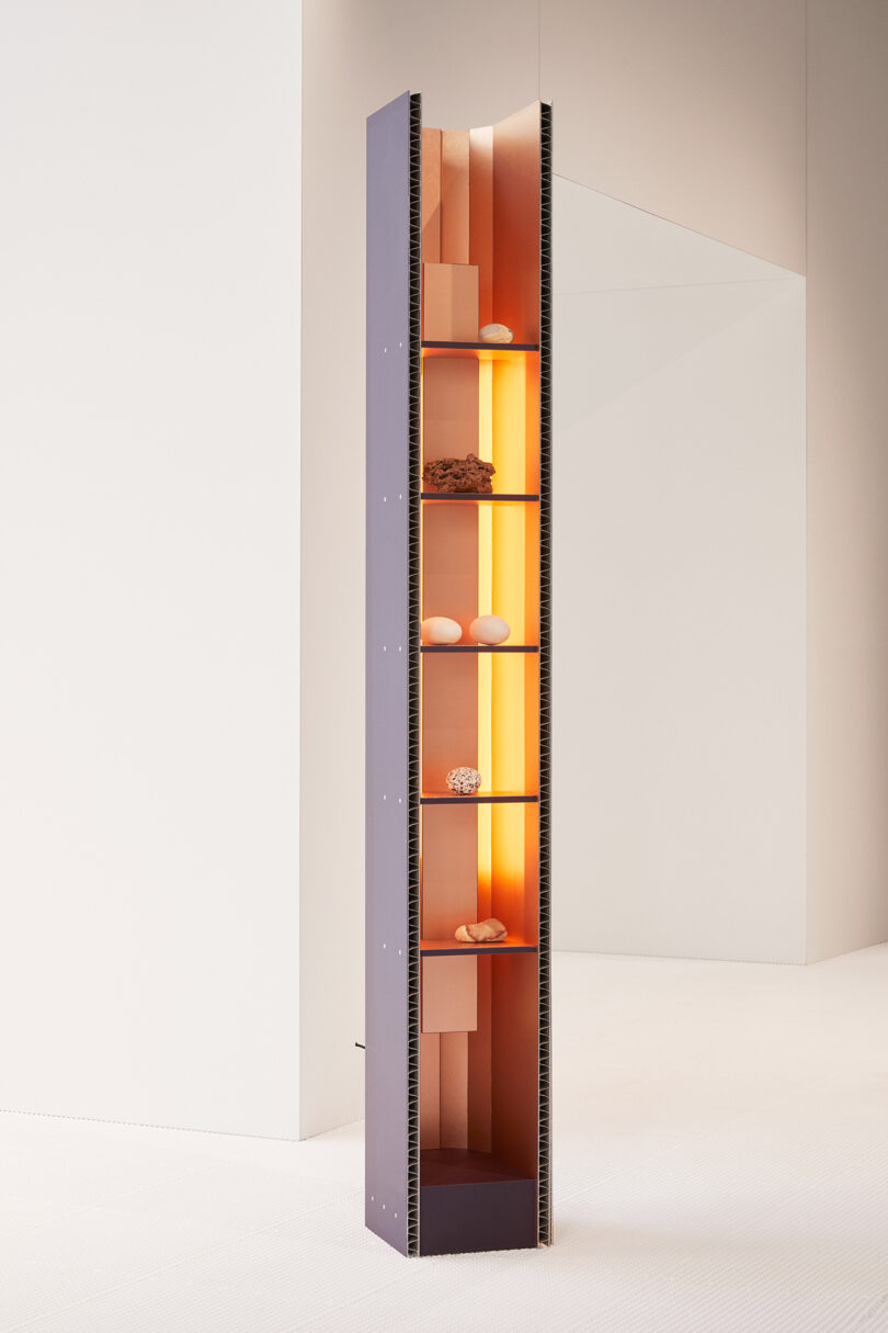 Tall, narrow vertical shelf with interior lighting and small decorative items on its shelves, set against a white background.