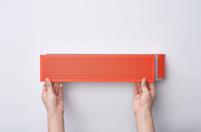 Hands holding a red perforated speaker front Vibrary Digital LP Player against a white background.