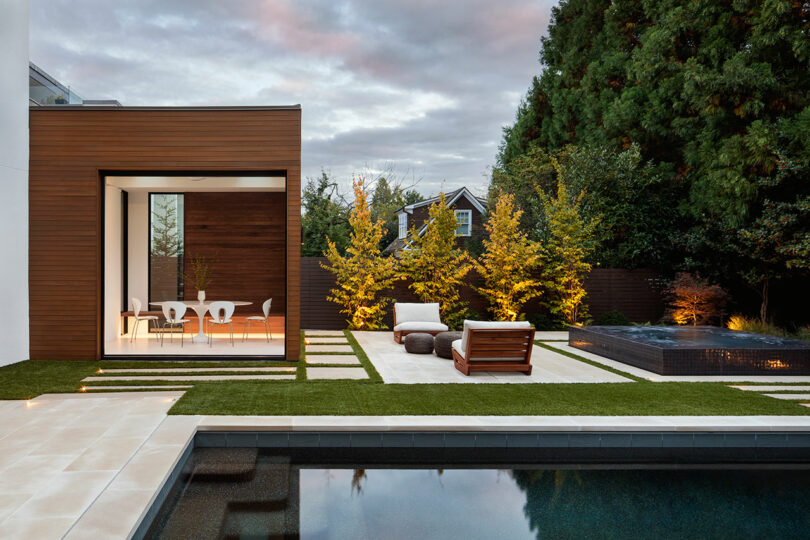 partial exterior view of modern wood paneled extension with eating area. Exterior features patio furniture with a pool and hot tub.