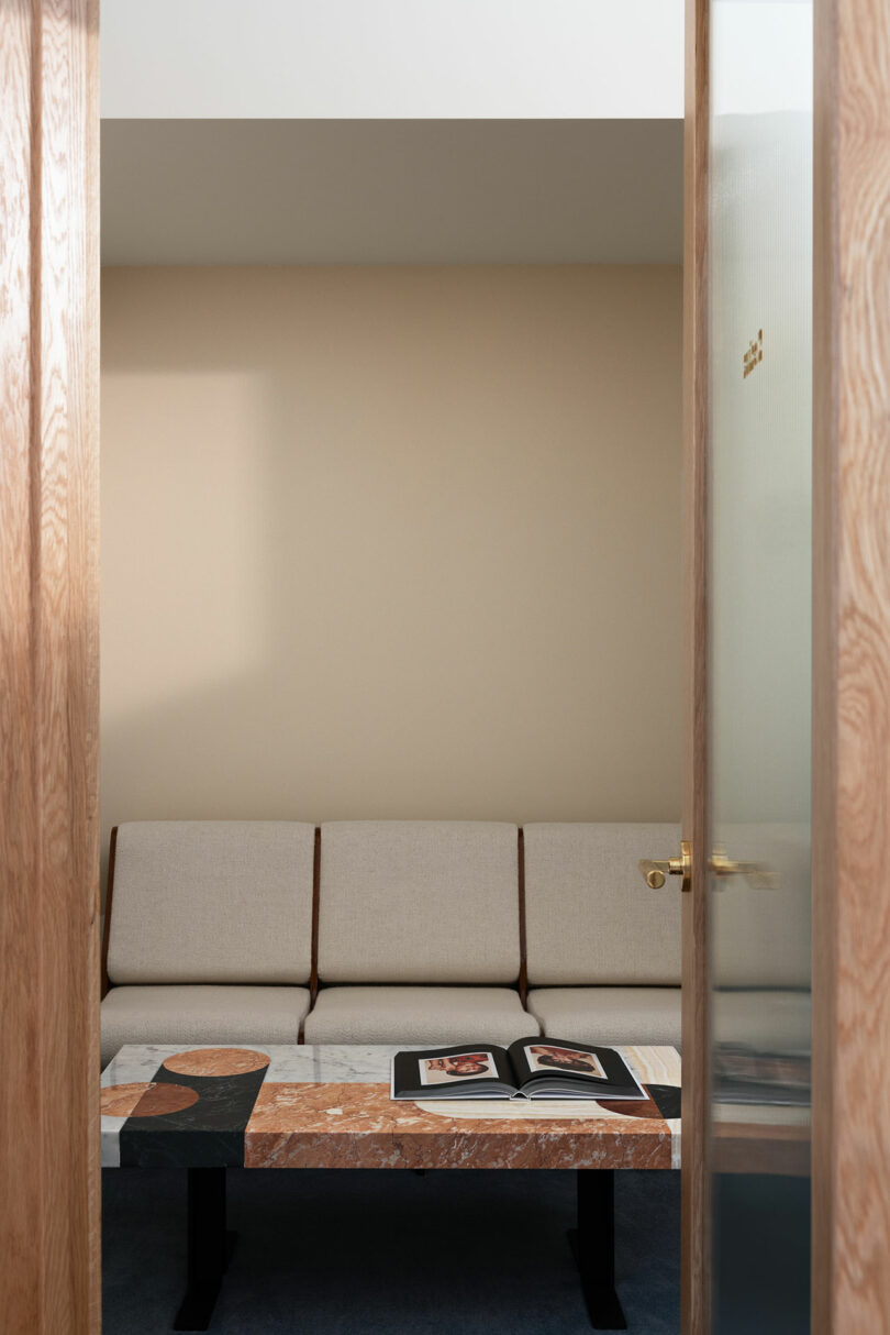 Modern living room with a beige sofa facing a small table with books, framed by wooden doorways with glass panels.