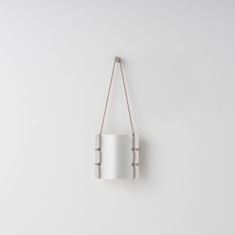 ceramic vase hanging on a white wall by a thread