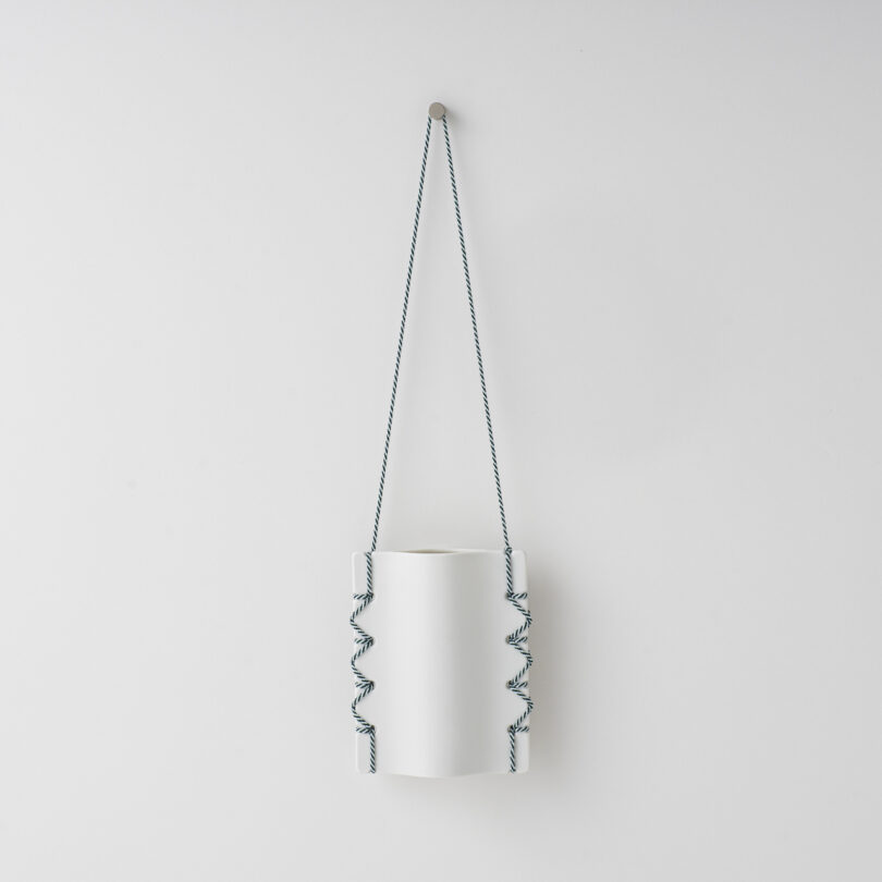 ceramic vase hanging on a white wall by a thread