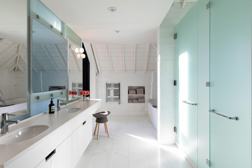 Modern bathroom with double sinks, large mirror, white tile walls, and frosted glass doors.