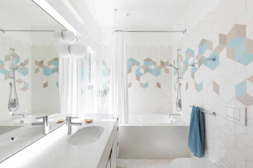 Modern bathroom interior featuring a double sink vanity, geometric tile walls, and a shower with a curtain. Bright lighting and minimal decor.