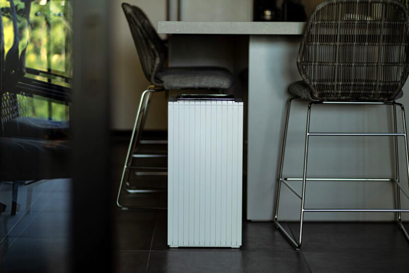 A modern room featuring a sleek portable radiator in the foreground, with stylish ZitA chairs and a table in the background, illuminated by natural light.