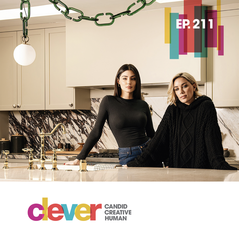 Two women standing at a modern kitchen island with green chain-link lighting hanging above.