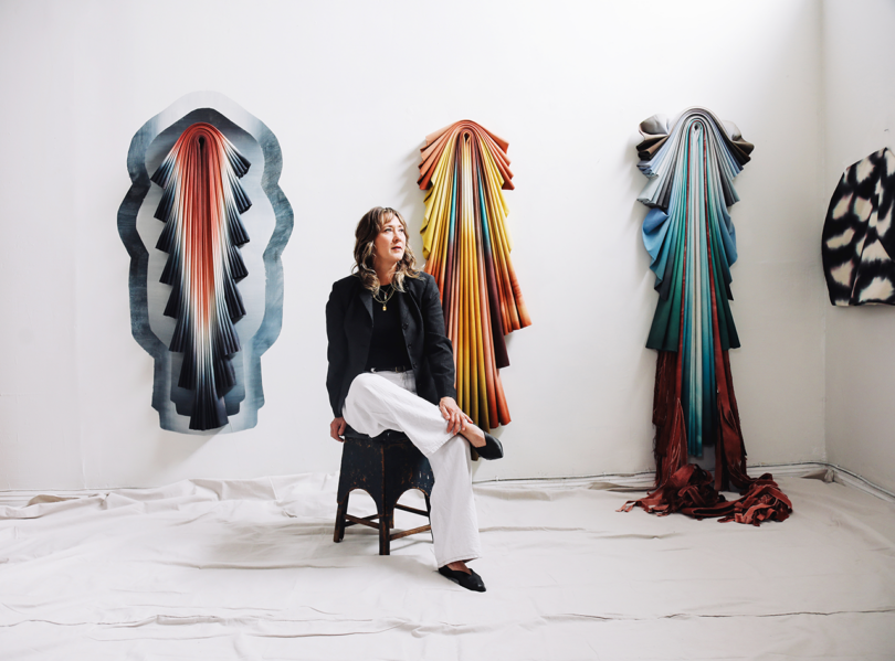 Woman sitting on a chair in a white room with colorful art on the walls.